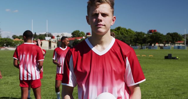 Confident Young Soccer Player Holding Ball on Field with Teammates - Download Free Stock Images Pikwizard.com