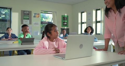 Elementary students collaborating with laptop and tablets in bright modern classroom