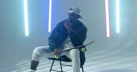 Stylish Young Man Holding Skateboard in Neon-Lit Studio Space