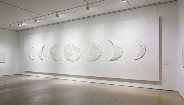 Minimalist museum installation featuring embossed moon phases on large white panel