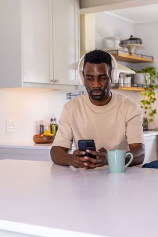African man wearing headphones using smartphone at kitchen counter with mint mug