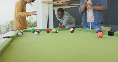 Young men playing pool in modern home game room around green felt table and smartphone