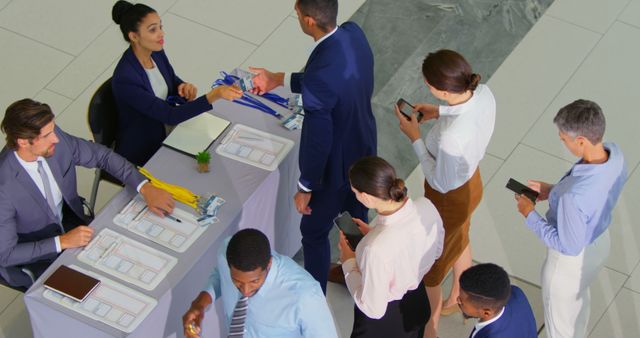 Business professionals queue at a check-in table to register for a conference. Name tags and lanyards are being distributed by staff. This image is great for illustrating networking events, corporate meetings, industry conferences, and professional gatherings.