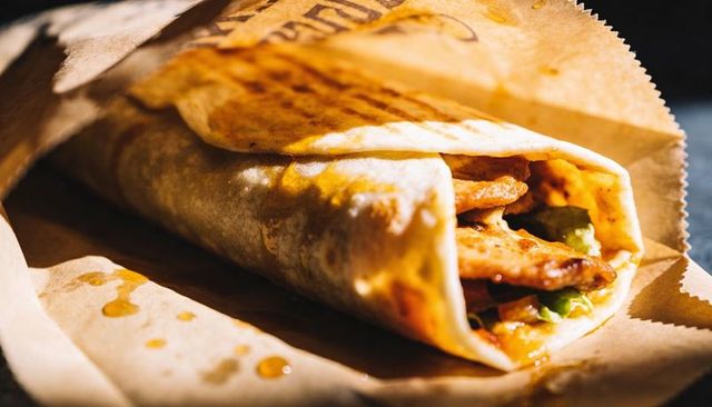 Grilled chicken tortilla wrap wrapped in kraft paper with savory sauce dripping and greens
