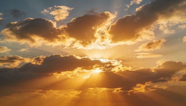 Golden crepuscular rays breaking through layered clouds at dramatic sunrise over horizon