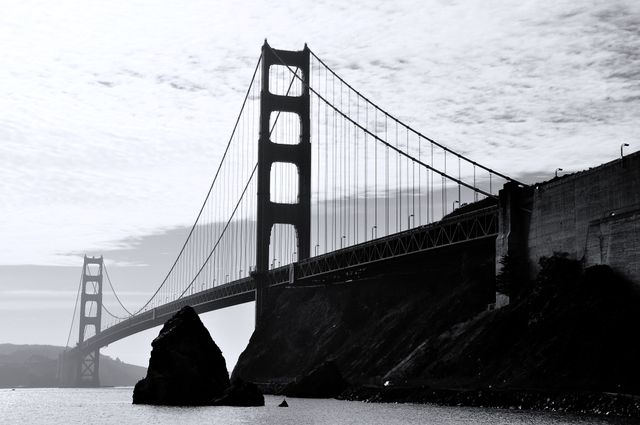 Black and white view of the stunning Golden Gate Bridge with clear sky and water. Ideal for travel blogs, architecture features, tourism brochures, and websites focusing on iconic landmarks. Adds a dramatic touch with its monochromatic scheme, perfect for emphasizing the architectural beauty and grandeur of the bridge.