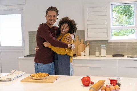 Couple hugging while baking pie in bright white kitchen, smiling and sharing warmth