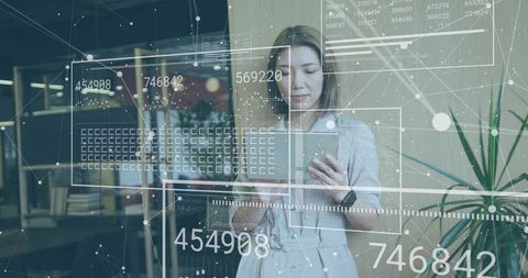 Asian professional holding tablet analyzing augmented reality data dashboard in office