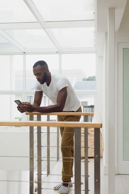 Side view of an African-American using a smartphone inside a white room with wood railings