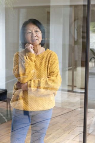 Thoughtful Senior Woman Pondering at Home Behind Glass