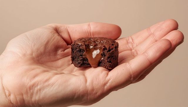 Elder hand presenting molten chocolate brownie with caramel center on neutral background