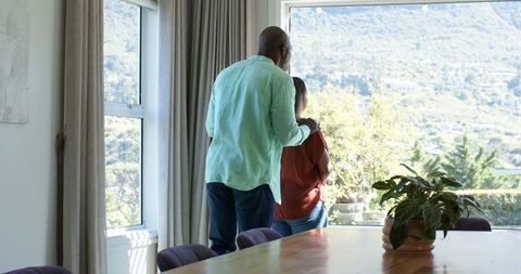 African american couple standing by sunlit window overlooking hillside from dining room