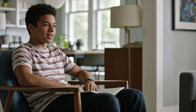 Teenager sitting in midcentury armchair holding spiral notebook planning homework