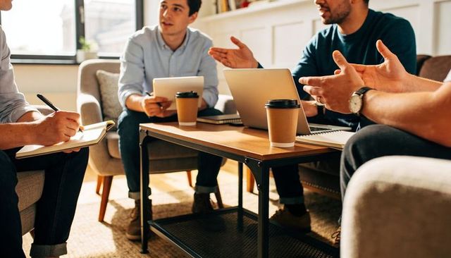 Small team discussing strategy in casual coworking lounge around low table with laptop