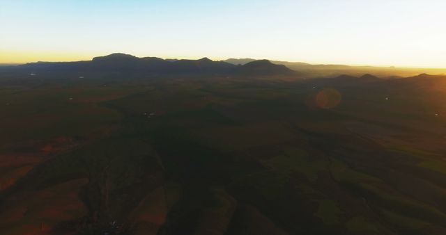 Beautiful aerial view featuring a vast mountain range and countryside bathed in the golden light of sunset. The horizon stretches endlessly, highlighting the serene natural beauty. Ideal for promoting travel, tourism, mountain resorts, or using in nature-themed projects and publications.