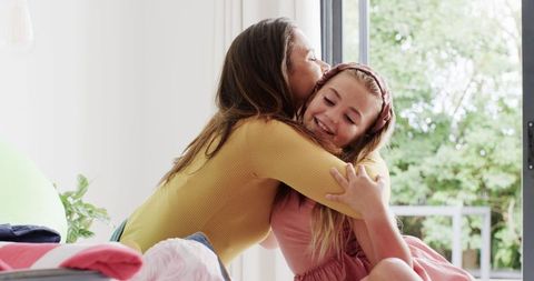 Mother and Daughter Embracing While Packing in Bright Bedroom