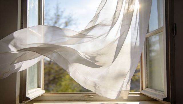 Billowing sheer curtain flowing through open window over weathered sill