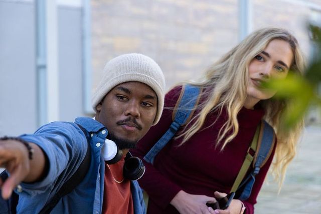 Young friends pointing while navigating with smartphone, backpacks and headphones outdoors