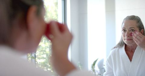 Mature Woman Applying Makeup in Modern Bathroom Mirror