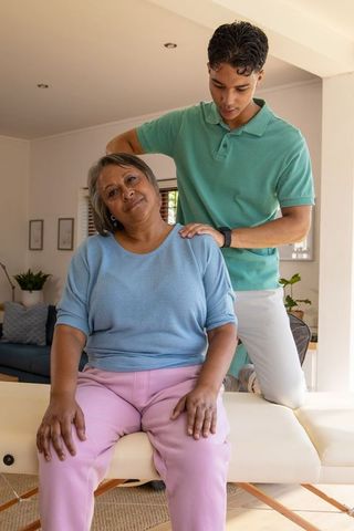 Male Caregiver Giving Shoulder Massage to Senior Woman for Wellness