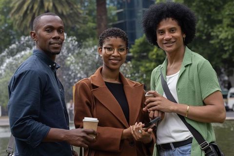 African american friends standing and smiling while holding coffee by city fountain