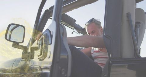 Man leaning into open-top suv roadside wearing striped tank top and sunglasses