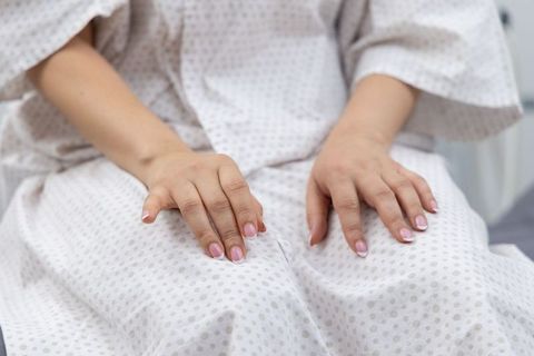 Patient sitting on clinic chair wearing polka-dot medical gown resting hands with french manicure