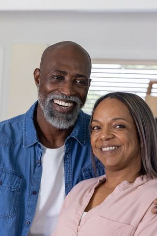 Smiling mature african american couple embracing at home near window blinds, cozy warmth