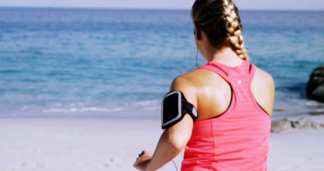 Fit woman putting music on mobile phone before jogging on the beach