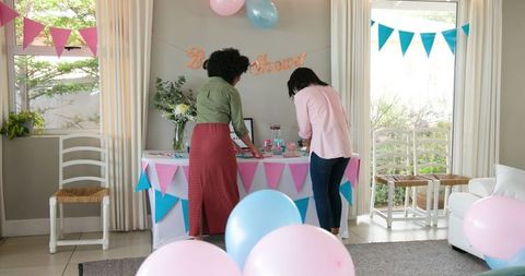 Two Women Preparing Colorful Baby Shower Celebration in Bright Living Room