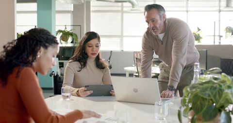 Diverse team collaborating around table using tablet and laptop in accessible office