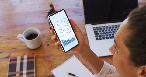 Businesswoman analyzing statistics on smartphone at desk