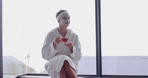 Woman Enjoying Spa Day with Facial Mask and Tea by Window