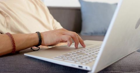 Man typing on silver laptop on sofa remote work casual home office hands with bracelets