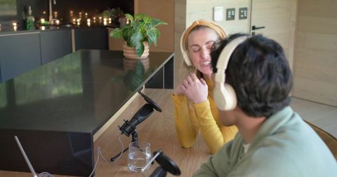 Young cohosts recording podcast at kitchen island with microphones and headphones