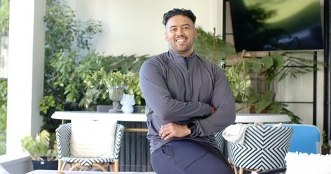 Confident african american man smiling in sunlit lounge wearing smartwatch and athleisure