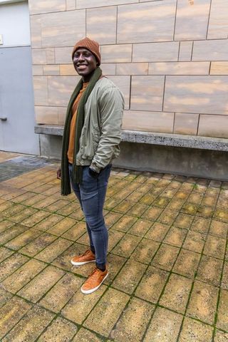 Urban autumn fashion: smiling young man wearing beanie, scarf, bomber jacket, sneakers