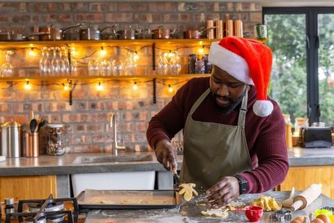 Man in santa hat placing homemade cookies on tray in festive kitchen holiday baking