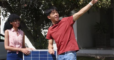 Asian man and black woman installing solar panel at home driveway, pointing and consulting