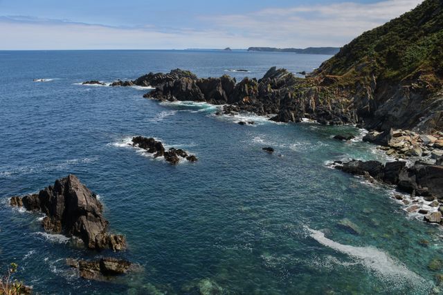 Beautiful view of a rocky coastline with sharp cliffs and clear blue ocean waters. Ideal for travel brochures, nature websites, or as artwork showcasing coastal beauty. Perfect for use in environments promoting serenity, natural landscapes, and adventure.