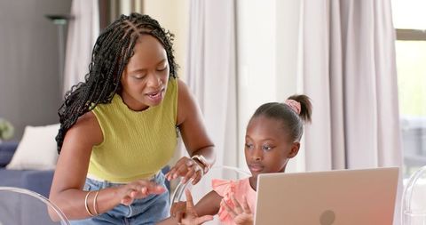 African mother teaching daughter counting with hands at laptop, homeschooling and mentoring