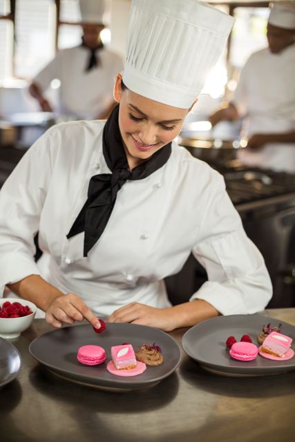 Smiling female chef finishing dessert plates in commercial kitchen