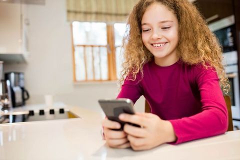 Happy Girl Using Smartphone in Cozy Kitchen at Home
