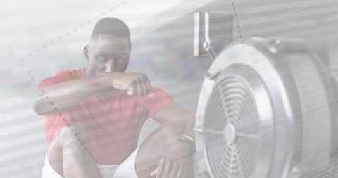 Tired gym athlete catching breath after intense rowing workout with fan cooling down
