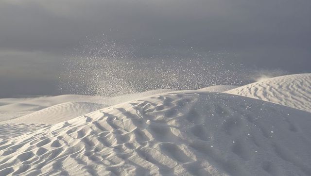 Windblown white dune spraying fine sand over minimalist overcast desert horizon