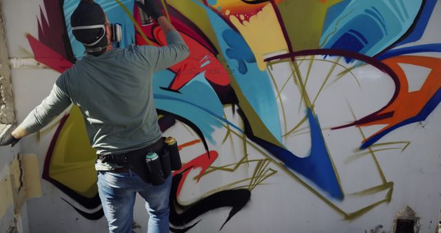 Rear view of Caucasian graffiti artist painting with aerosol spray on the wall. He is wearing protective mask 4k