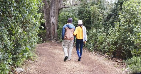 Walking arm-in-arm on leafy gravel trail during autumn, diverse couple enjoying nature