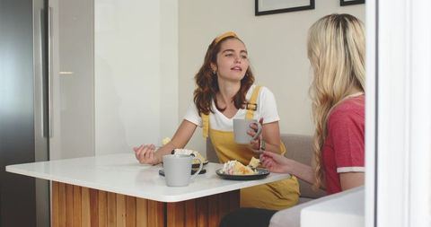 Young women chatting over coffee and cake at kitchen island, casual home lifestyle