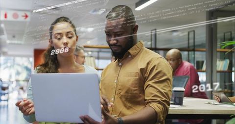 Diverse colleagues collaborating over laptop with code overlay in modern open office
