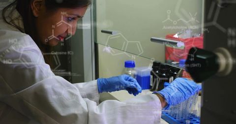 Laboratory technician handling samples wearing lab coat and blue gloves under glass shield